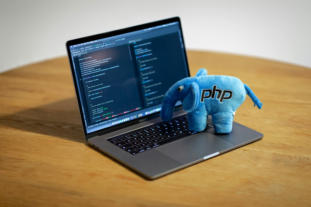 Ein Laptop zeigt zwei PHP-Code-Fenster, auf der Tastatur steht ein blauer Plüsch-Elefant mit der Aufschrift "PHP".