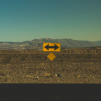 Leere Landschaft mit einer Straße und einem Schild, das nach links und rechts zeigt – symbolisiert die Entscheidung zwischen zwei Wegen.